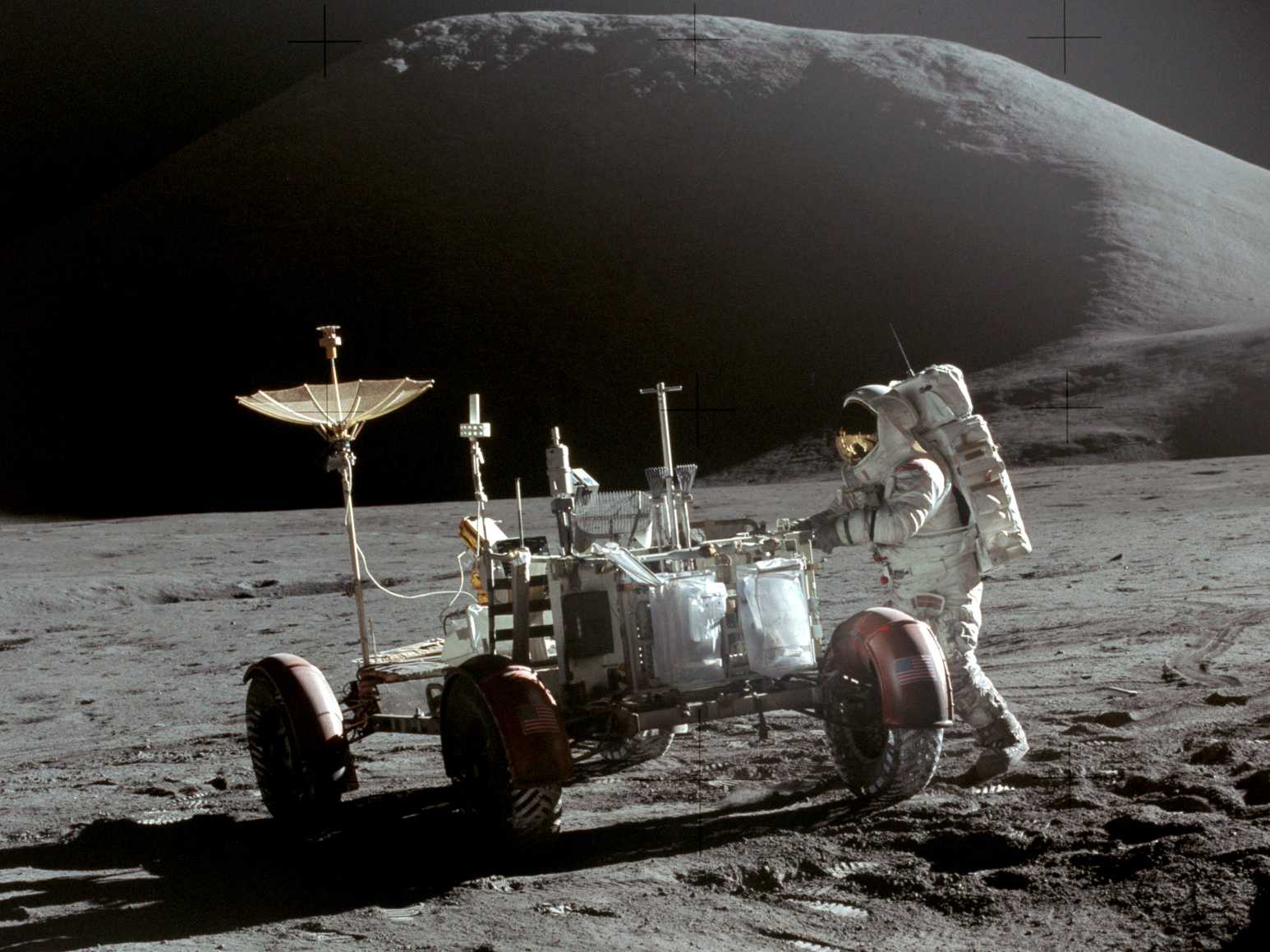 astronaut Jim Irwin stands next to the lunar rover on the moon, with a mountain in the background