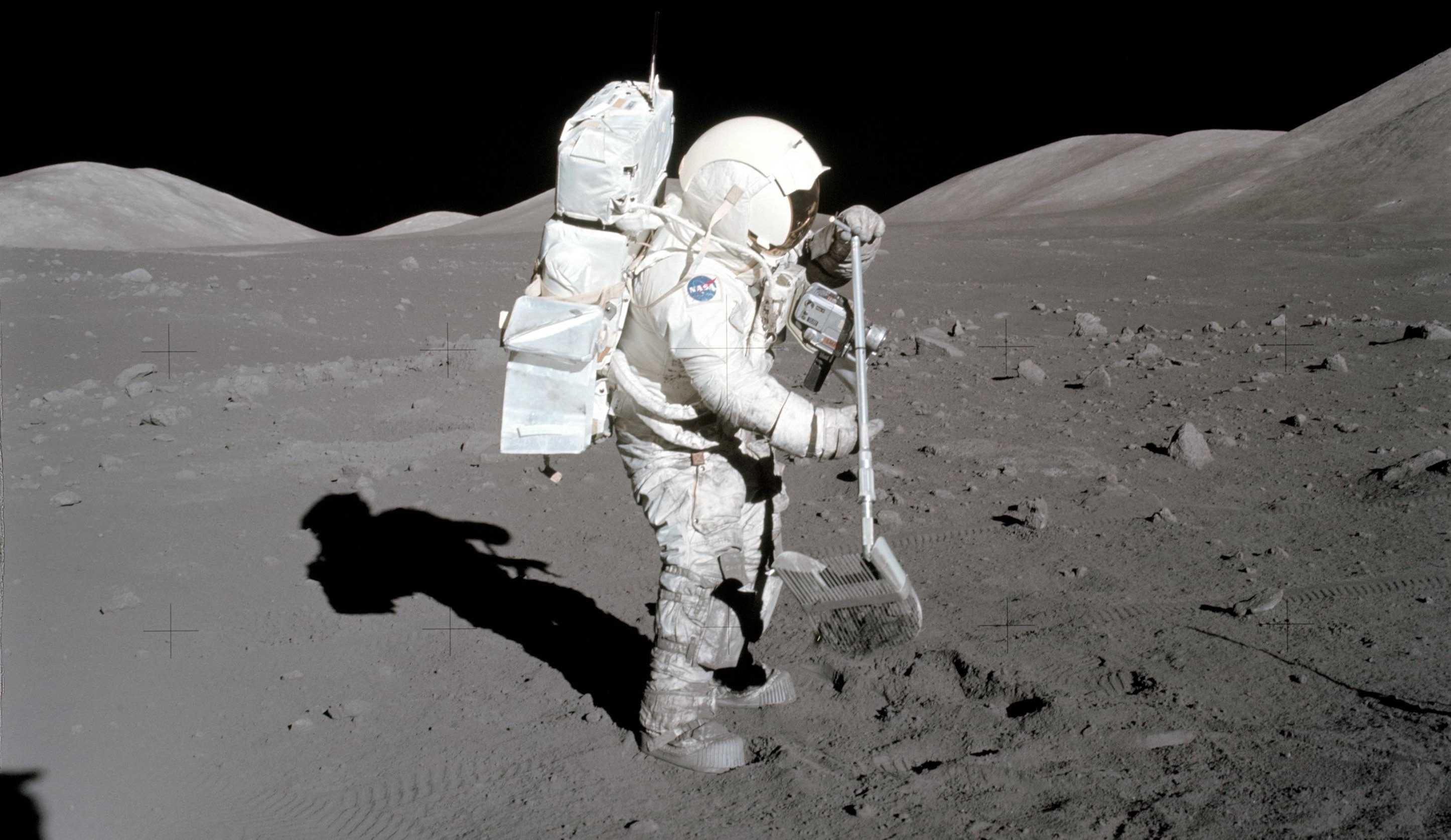 Harrison Schmitt on the Moon collecting surface samples with what looks like a rake mixed with a dustpan.